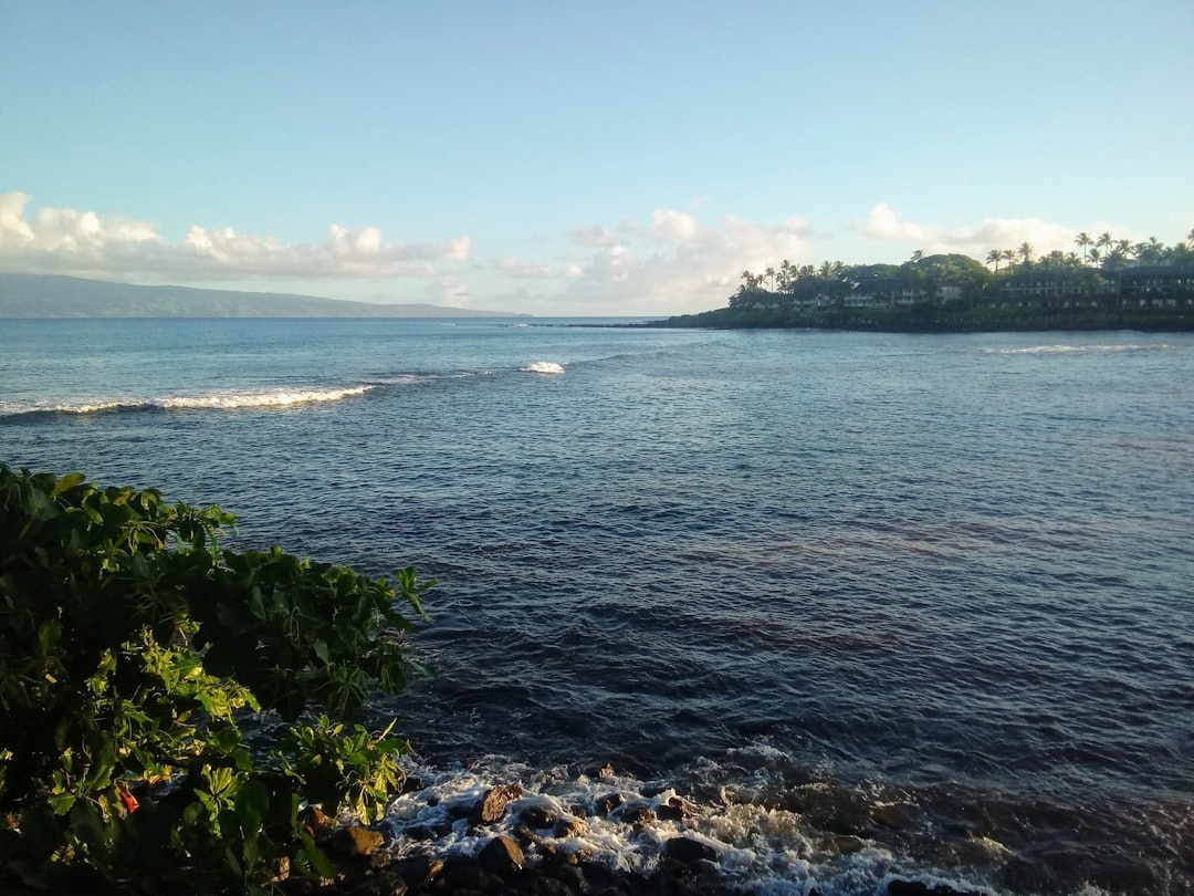 Swell breaking over the outer reef off a West Maui point, with a resort-lined headland on the right and Molokai on the horizon